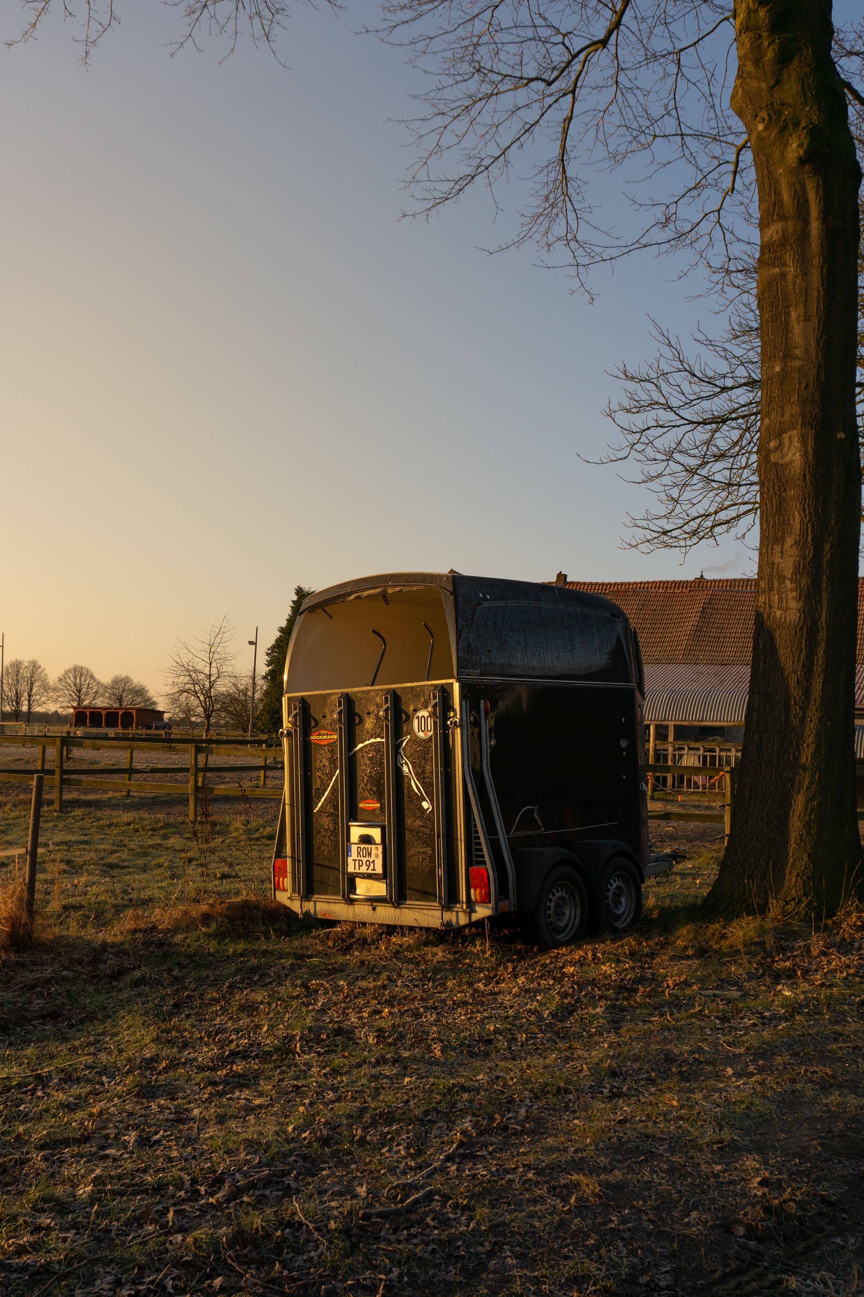 Livestock trailer parked under a tree at sunset